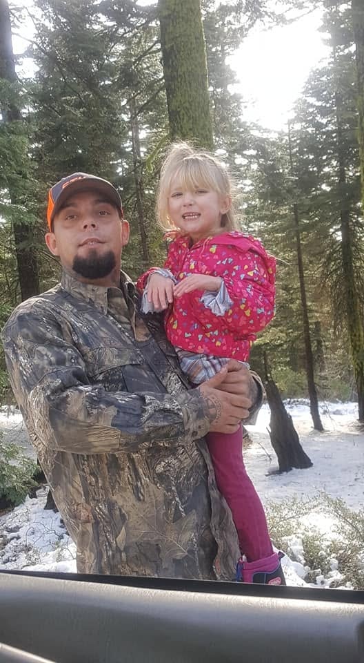 Adult holding a young child among snow-covered evergreens